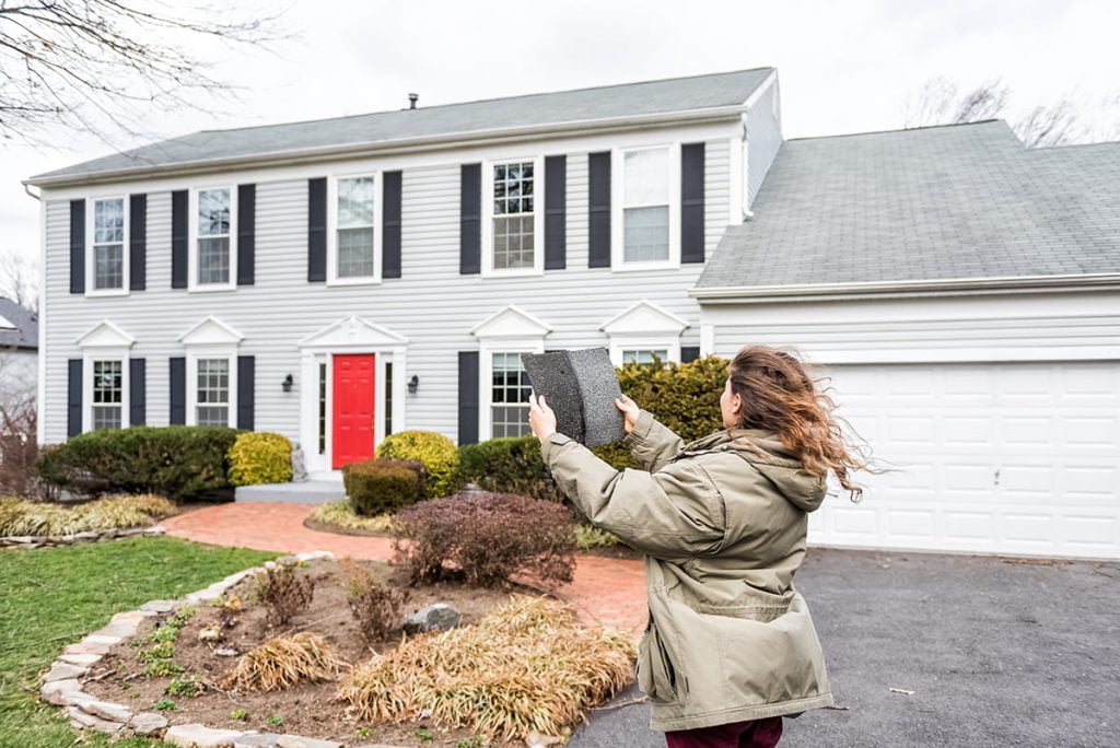 Young woman, female homeowner standing in front of house on wind
